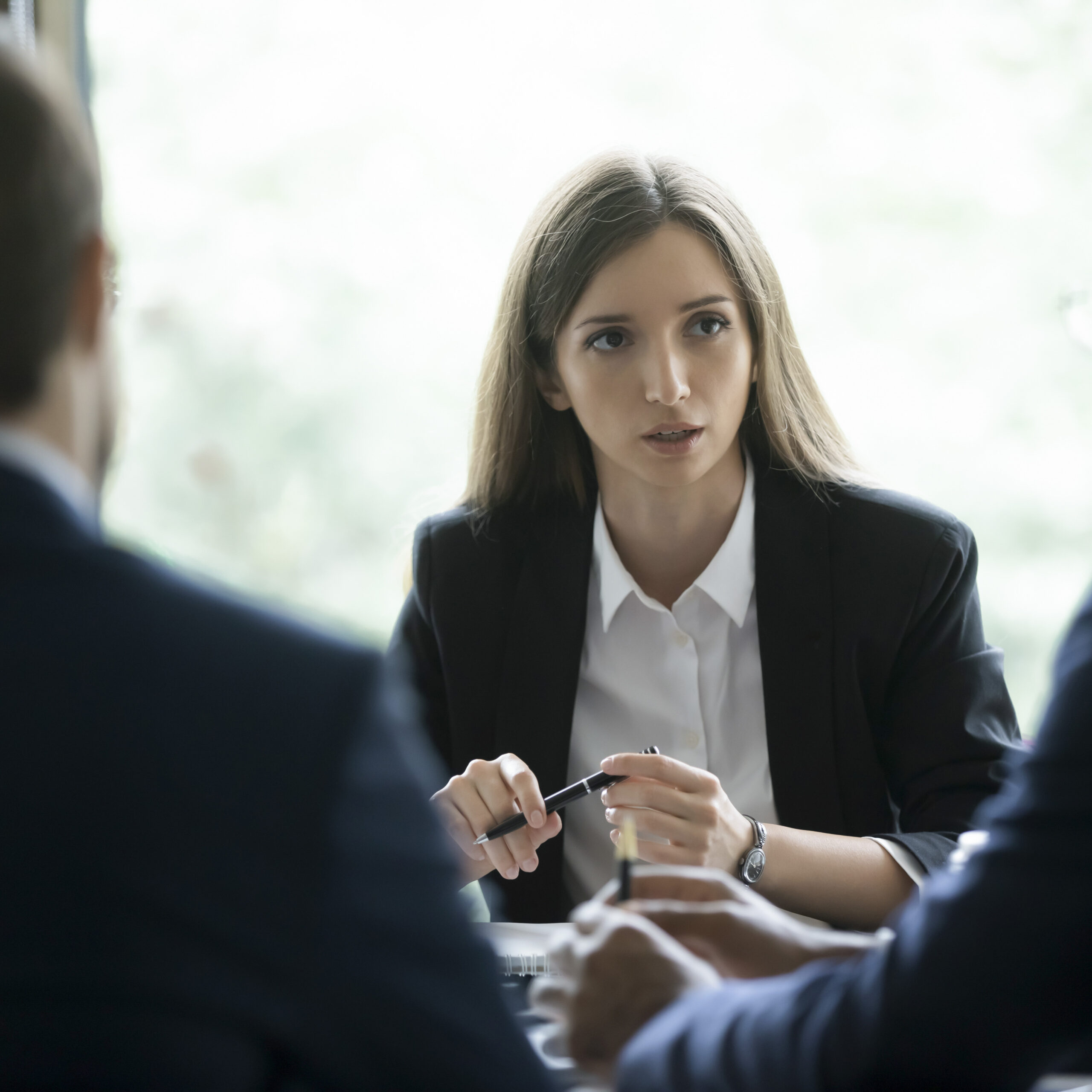Junge Frau im Business-Outfit spricht mit zwei Kollegen in einem professionellen Meeting-Setting