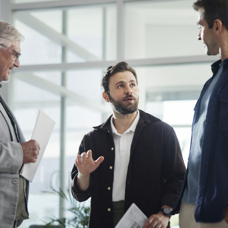 Drei Männer in einem lockeren Gespräch in einem modernen Bürogebäude mit Glasfront