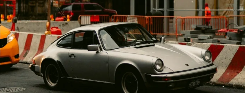 Ein Porsche steht vor einem Pfandleihhaus, mit Baustellenabsperrungen und Straßenbauarbeiten im Hintergrund.