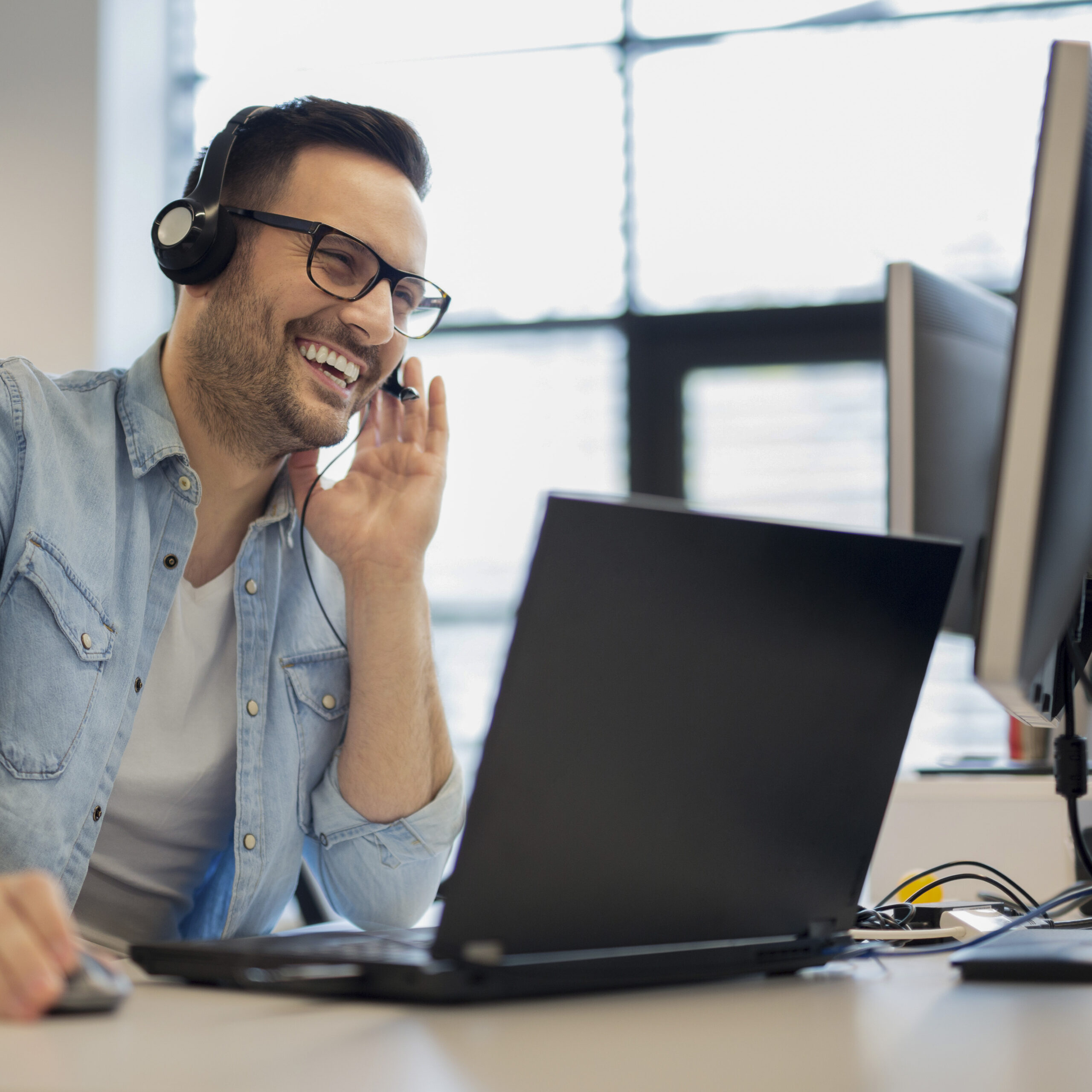 Ein Mann in einem Büro mit Kopfhörern lächelt während eines Telefongesprächs.