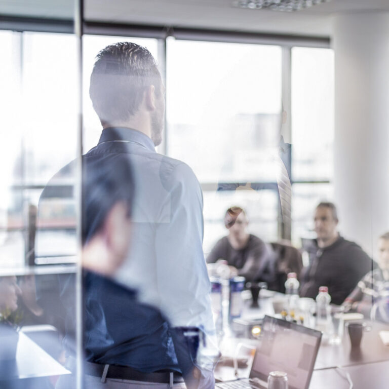 Ein Trainer steht vor einer Gruppe, die Notizen macht, in einem modernen Konferenzraum.