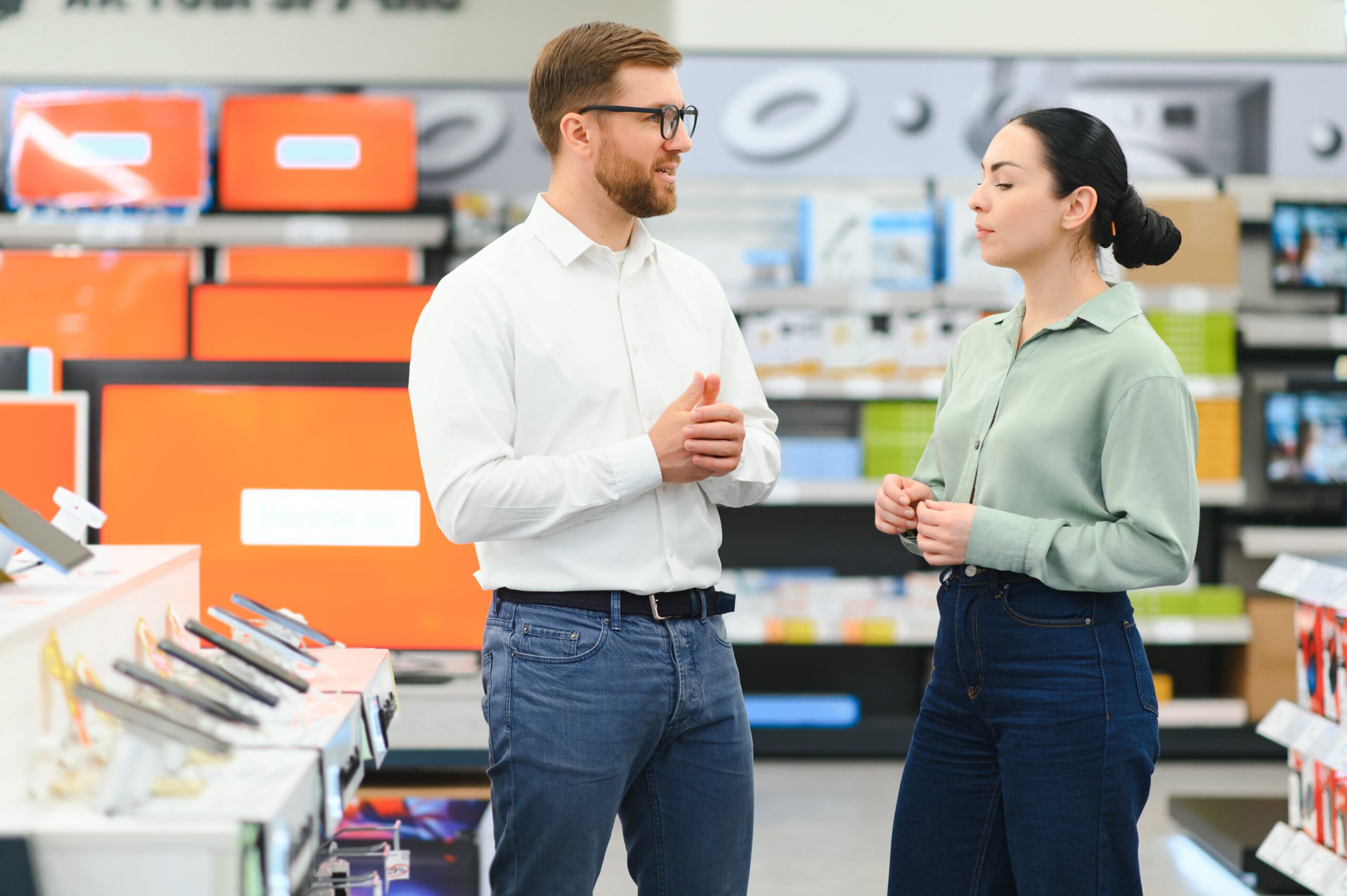 Verkäufer und Kundin im Gespräch zwischen Smartphone-Auslagen in einem Elektronikmarkt
