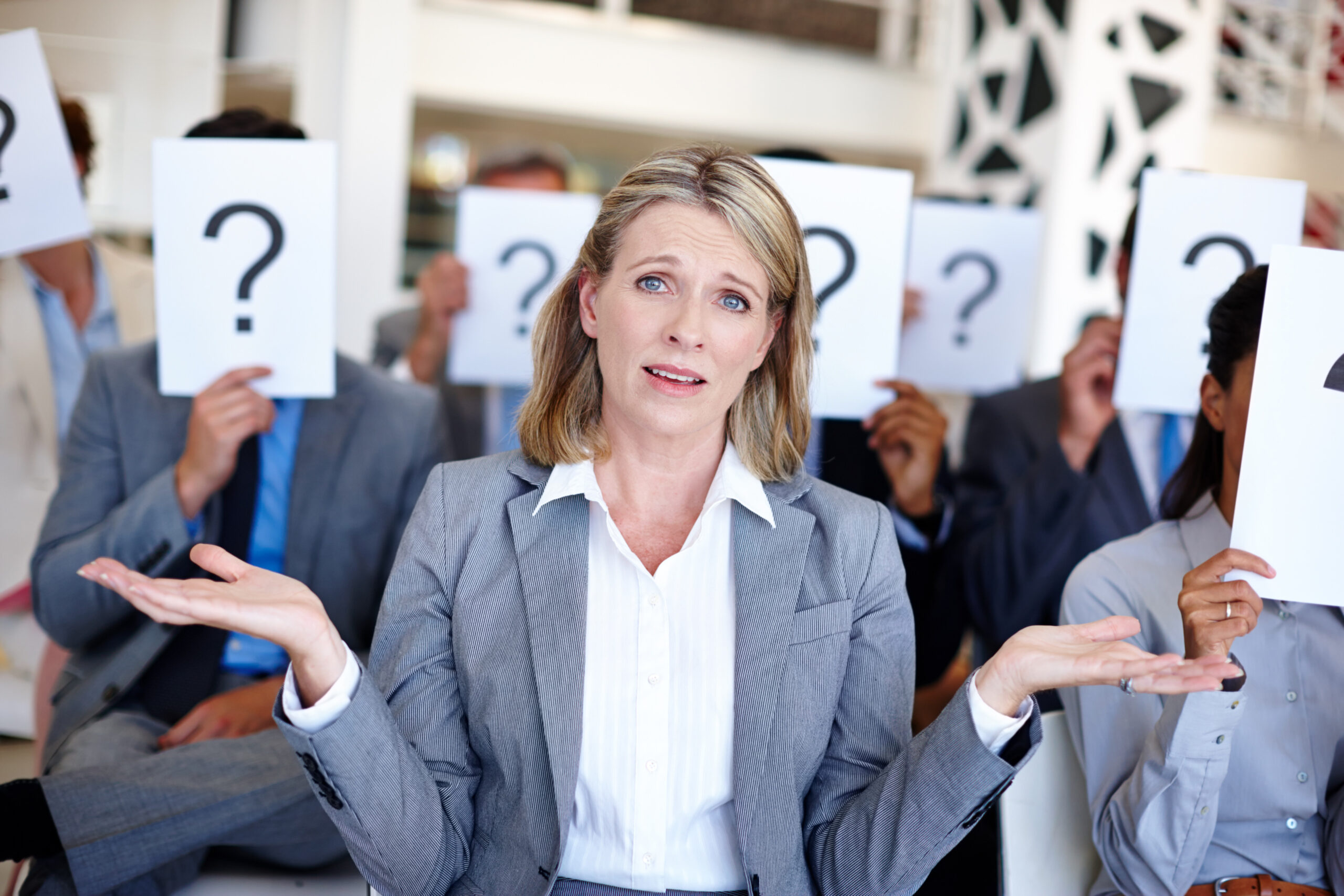 Ein Bild einer Frau mit vielen Menschen im Hintergrund, welche Fragezeichen vor dem Gesicht haben.